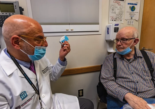 Miguel Divo shows his patient, Joel Rubinstein, a dry powder inhaler. It's an alternative to some puff inhalers that emit potent greenhouse gases, but is equally effective for many patients with asthma.