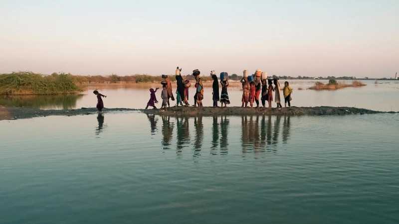 Children walking and carrying water in their head next to a source of water