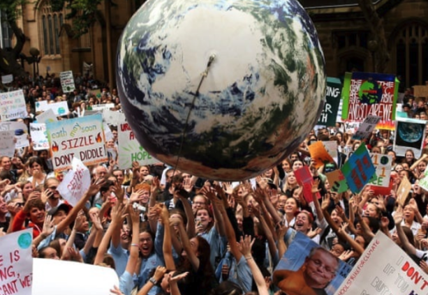 People gather with climate change signs and push a ballon with the shape of the earth into the earth